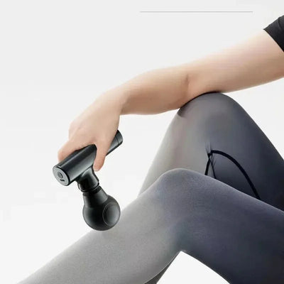 Person using a portable electric muscle massage gun on their leg for deep tissue relief.