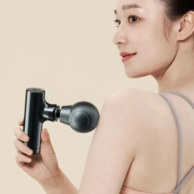 Woman using a portable electric muscle massage gun on her shoulder for deep tissue relief.